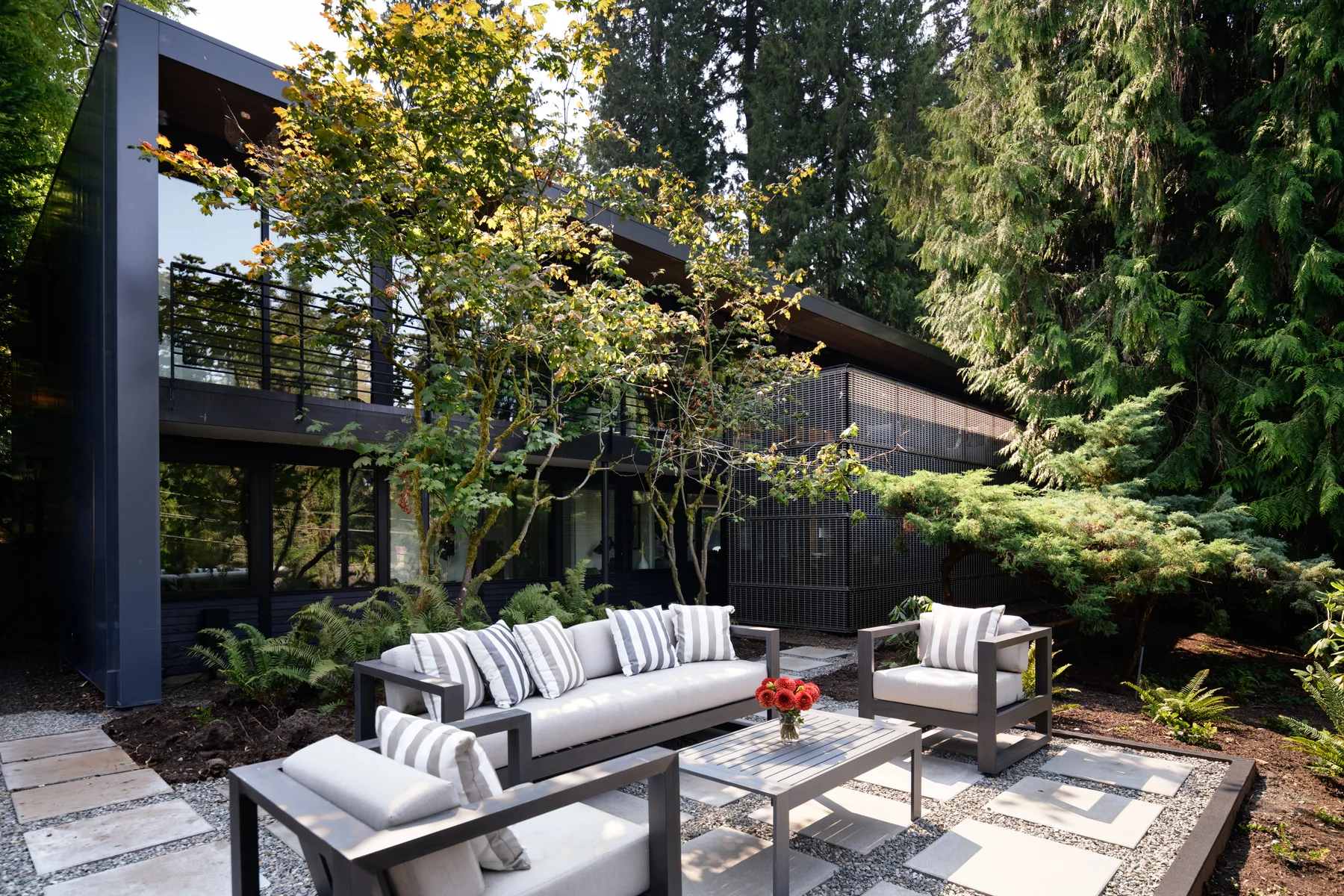 Modern black-clad Mercer Island home with an outdoor lounge and stone patio surrounded by evergreens