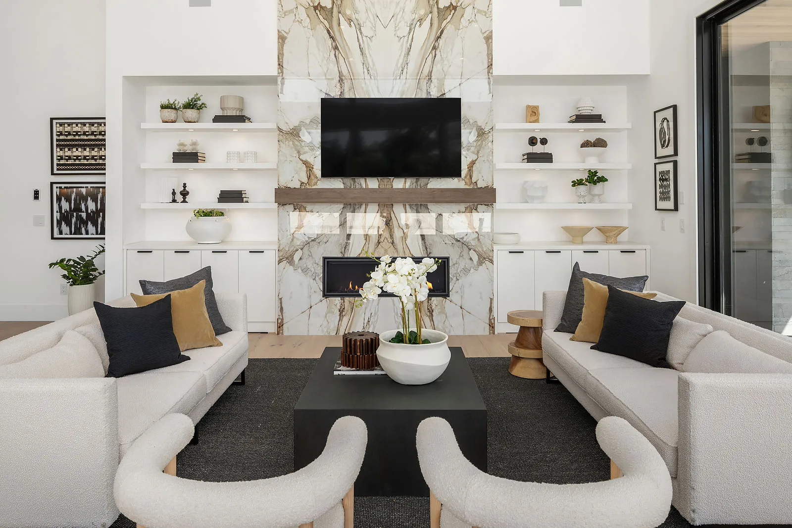Symmetrical living room view with floating shelves, a marble fireplace, and curved bouclé chairs around a black coffee table
