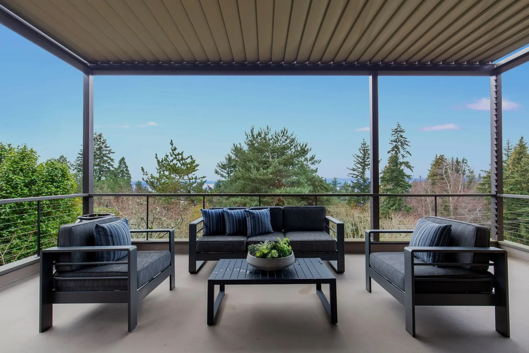 Covered deck staged with a black outdoor sofa set and striped pillows overlooking the treetops and Puget Sound