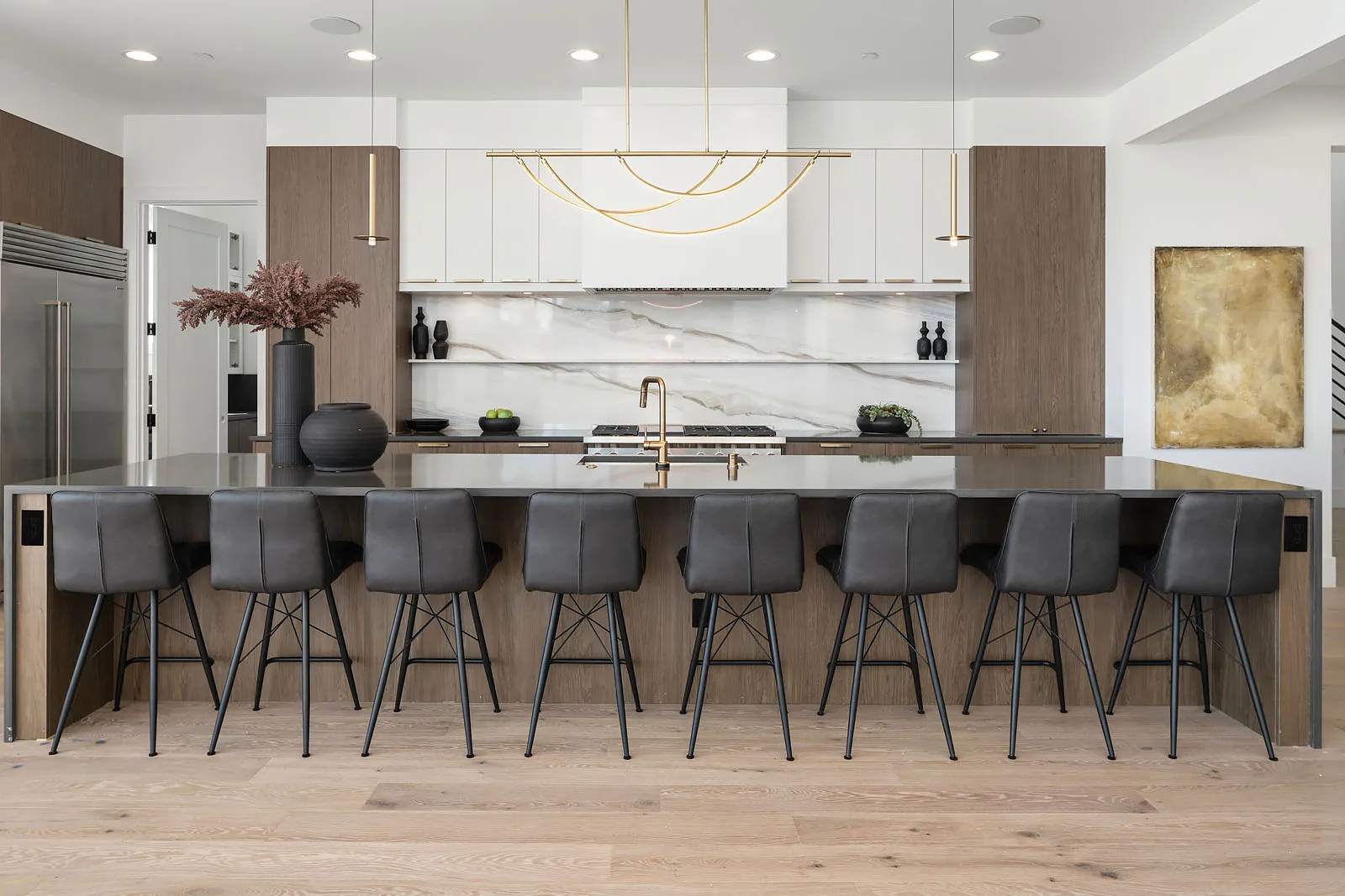 Open kitchen with a long island lined with leather barstools, walnut cabinetry, and a marble slab backsplash