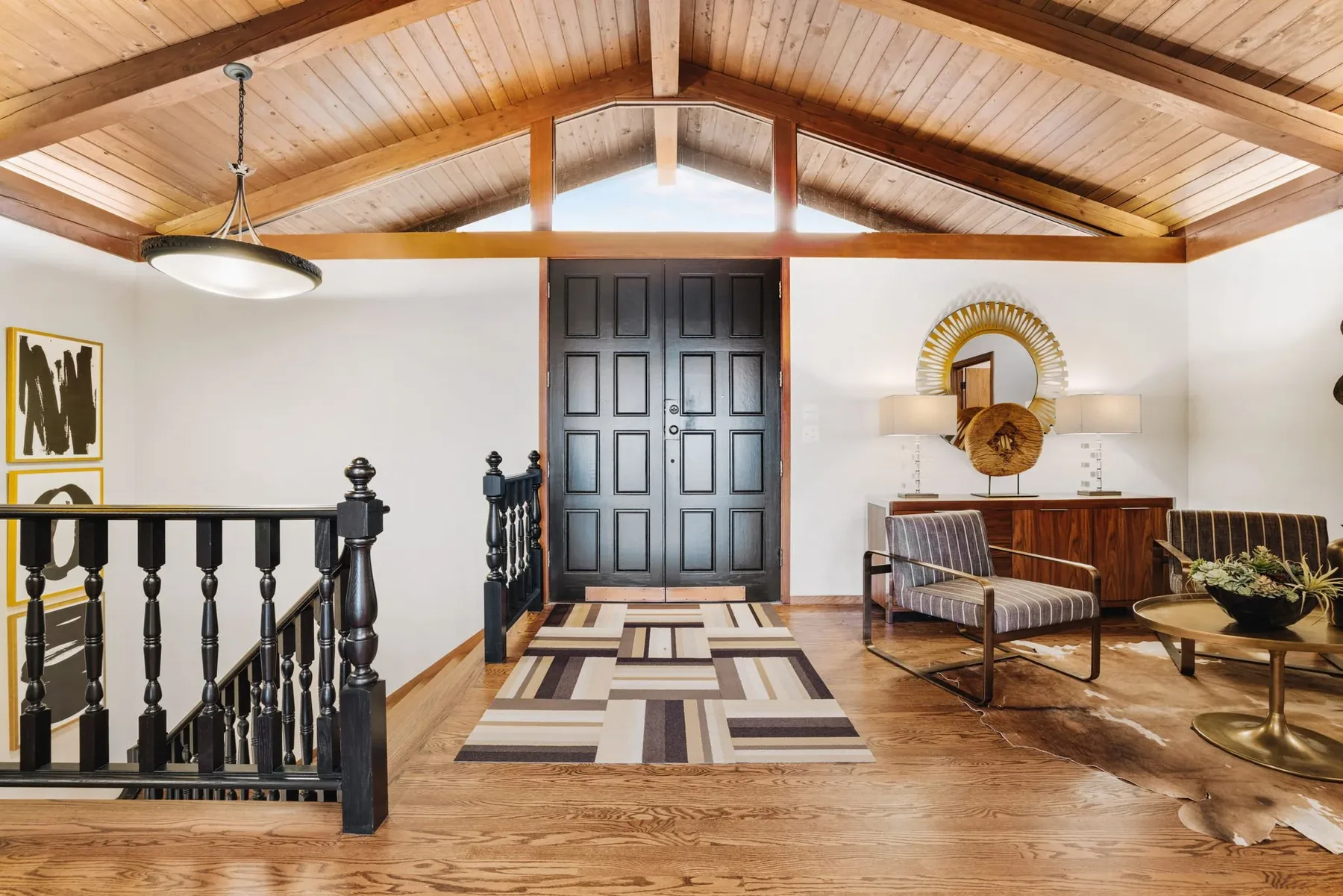Mid-century entry foyer staged by RD Interiors with a turned-baluster staircase, double doors, and a graphic area rug
