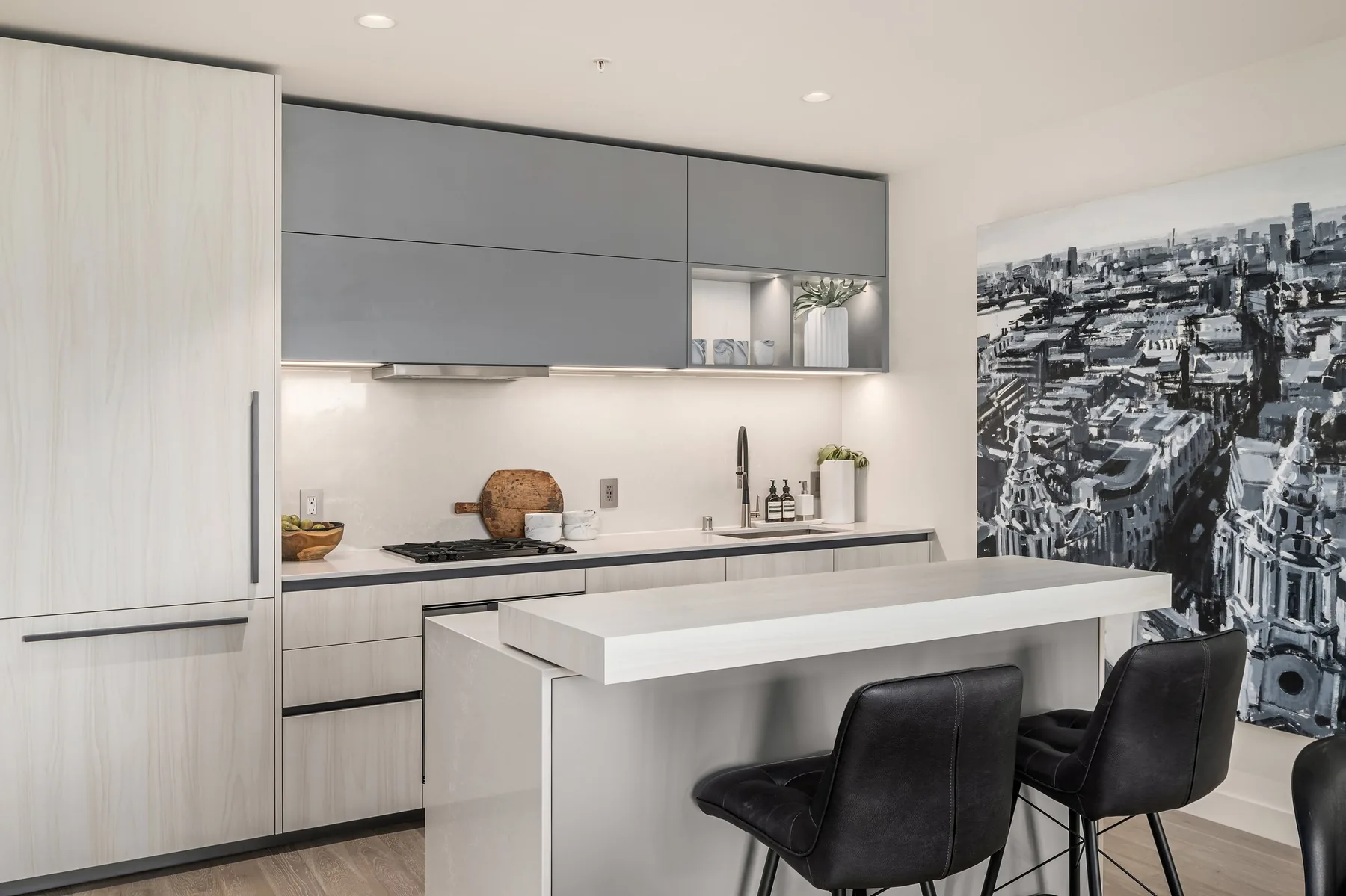 Luxury listing staging with a modern condo kitchen, waterfall island, grey cabinetry, and a black-and-white cityscape mural