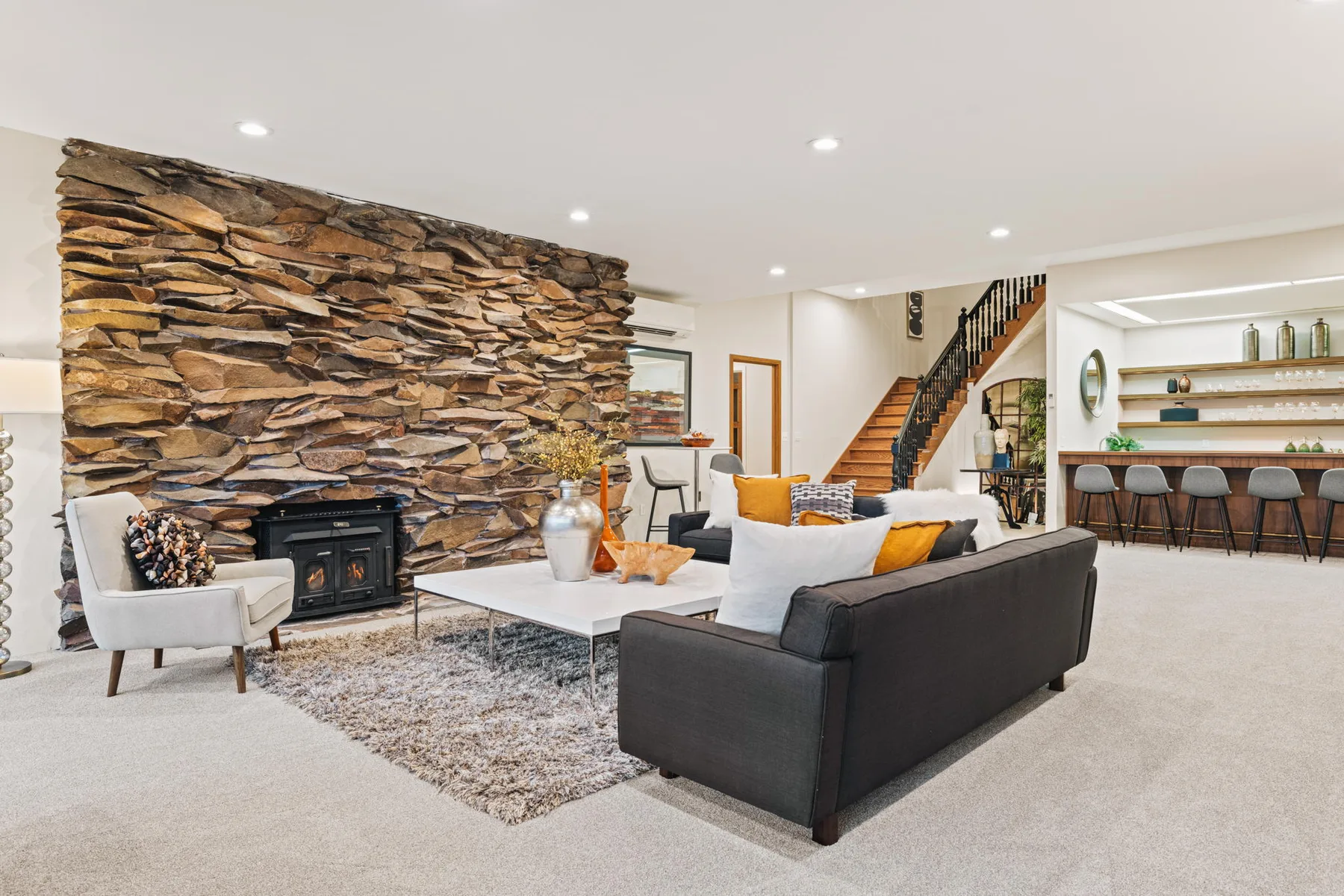 Lower-level family room with a floor-to-ceiling stone fireplace and a staircase beyond