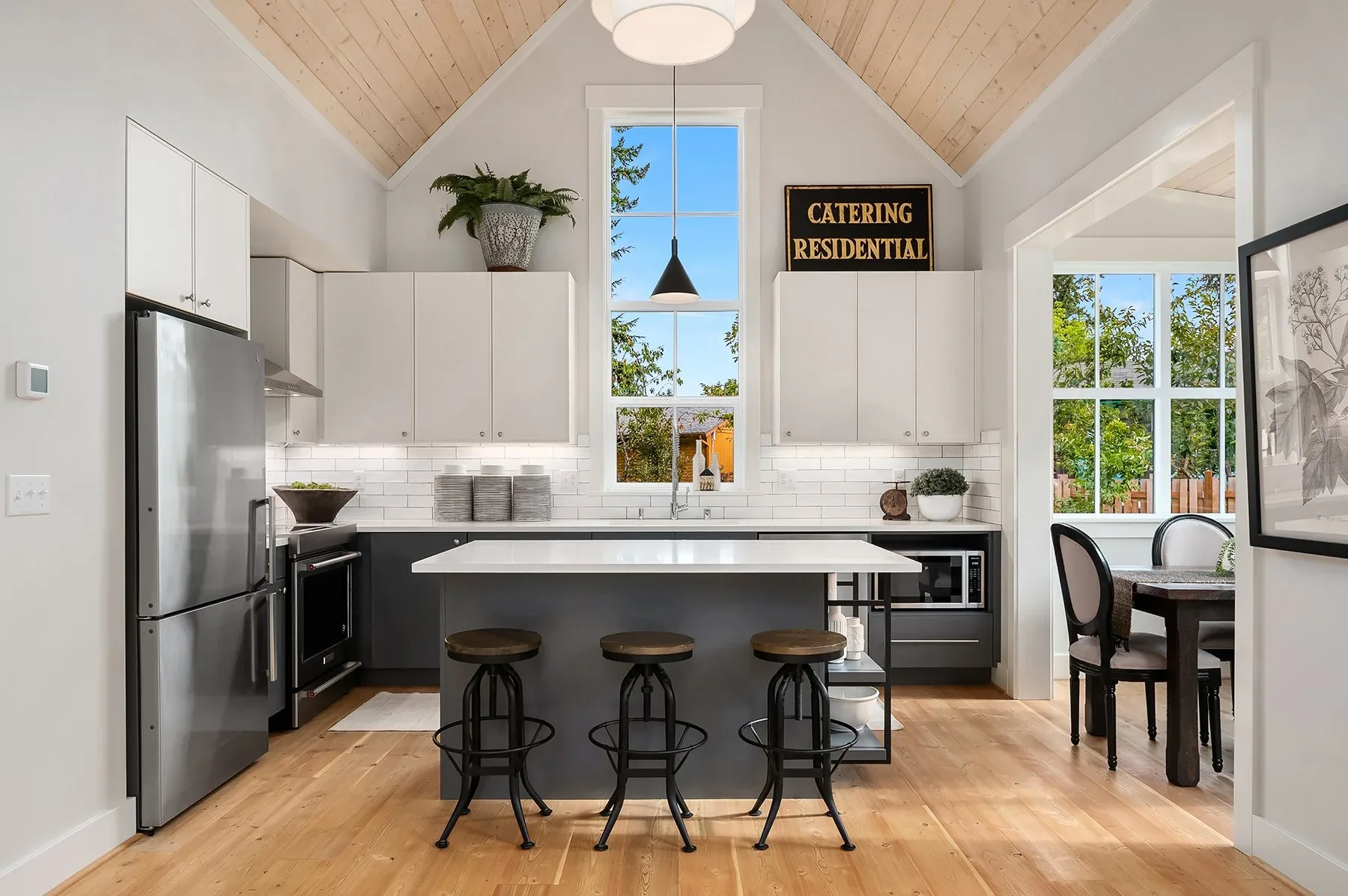 Kitchen staged by RD Interiors with a gray island, industrial bar stools, white cabinetry, and a soaring cedar-plank vaulted ceiling