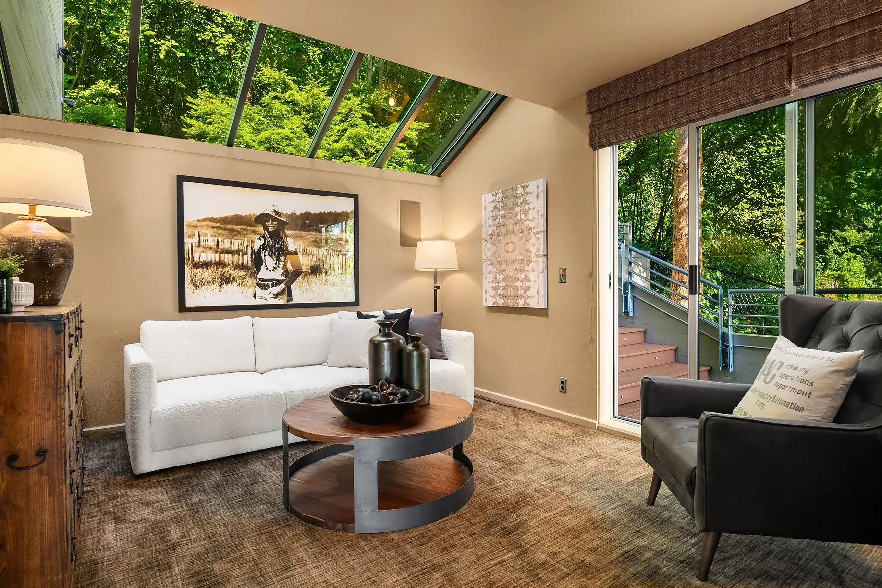 Sunroom staged by RD Interiors with a white loveseat, skylit sloped ceiling, and sliding doors to a deck among the trees