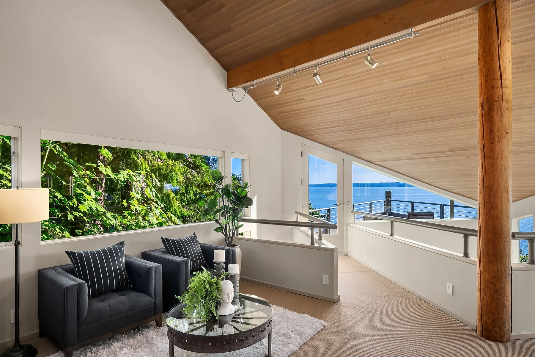 Upstairs loft sitting area staged with navy armchairs, a cedar-plank vaulted ceiling, and a railing overlooking the water