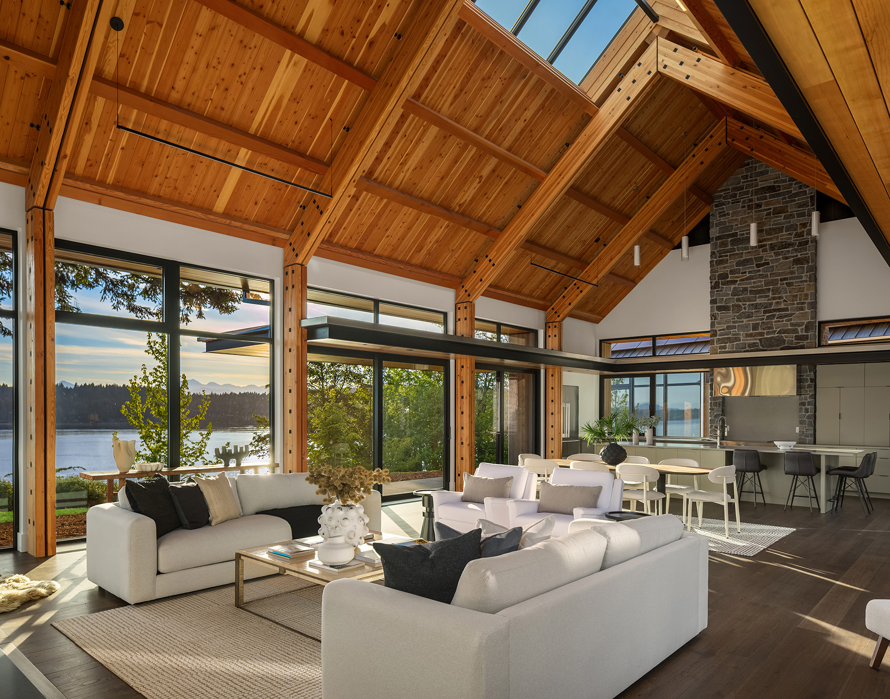 Waterfront great room with exposed timber beams, skylights, and a staged living area flowing into the kitchen
