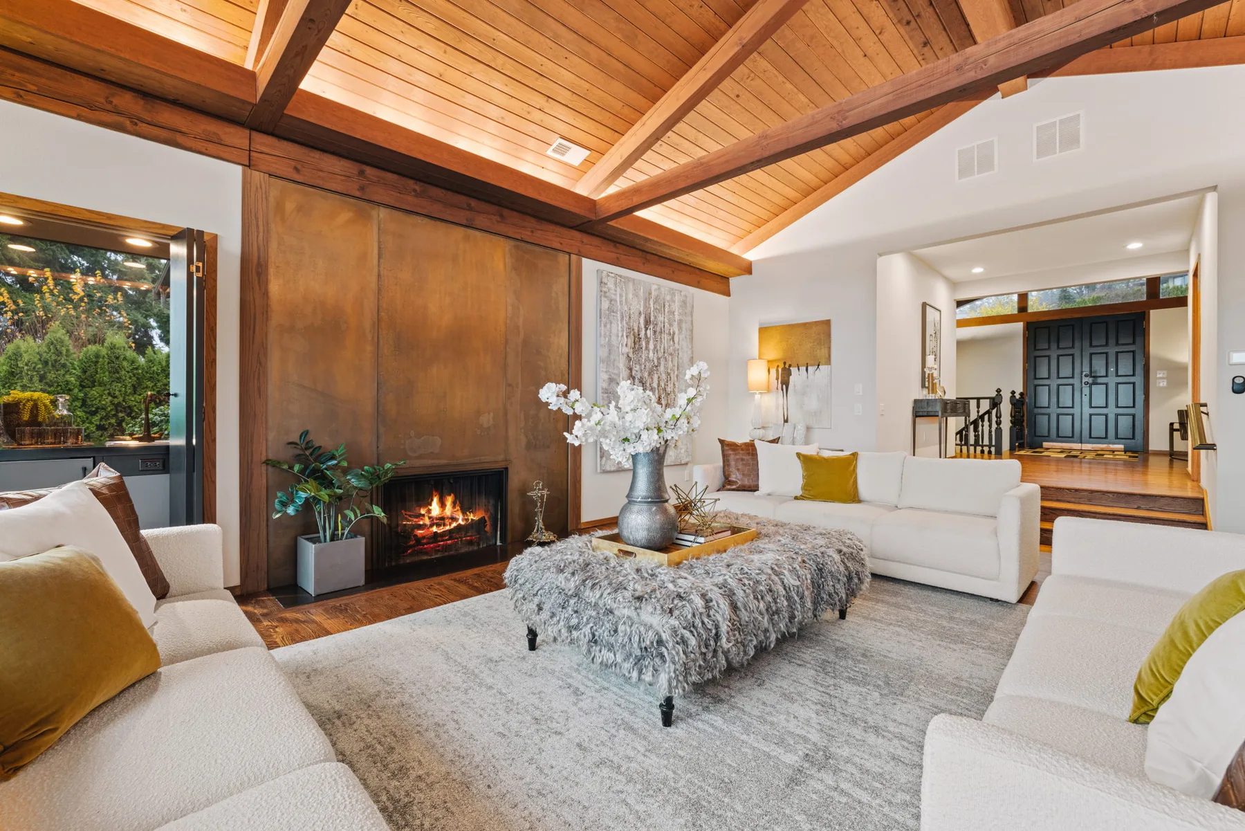 Fireside living room with wood paneling, a stone hearth, and a textured ottoman