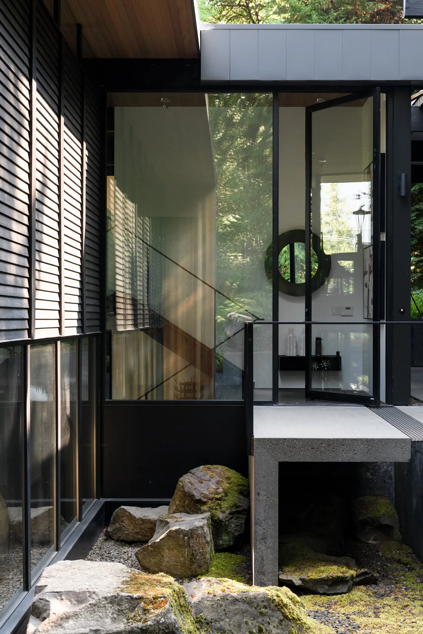 Luxury home staging featuring a glass-walled entry bridge over a sculpted rock garden in a modern Mercer Island home