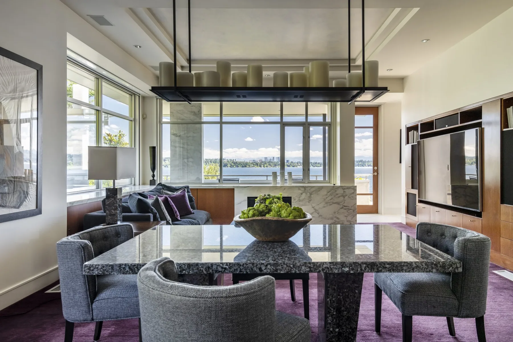 Kitchen dining area staged by RD Interiors with a granite table, gray chairs, a plum rug, and a marble island overlooking the lake
