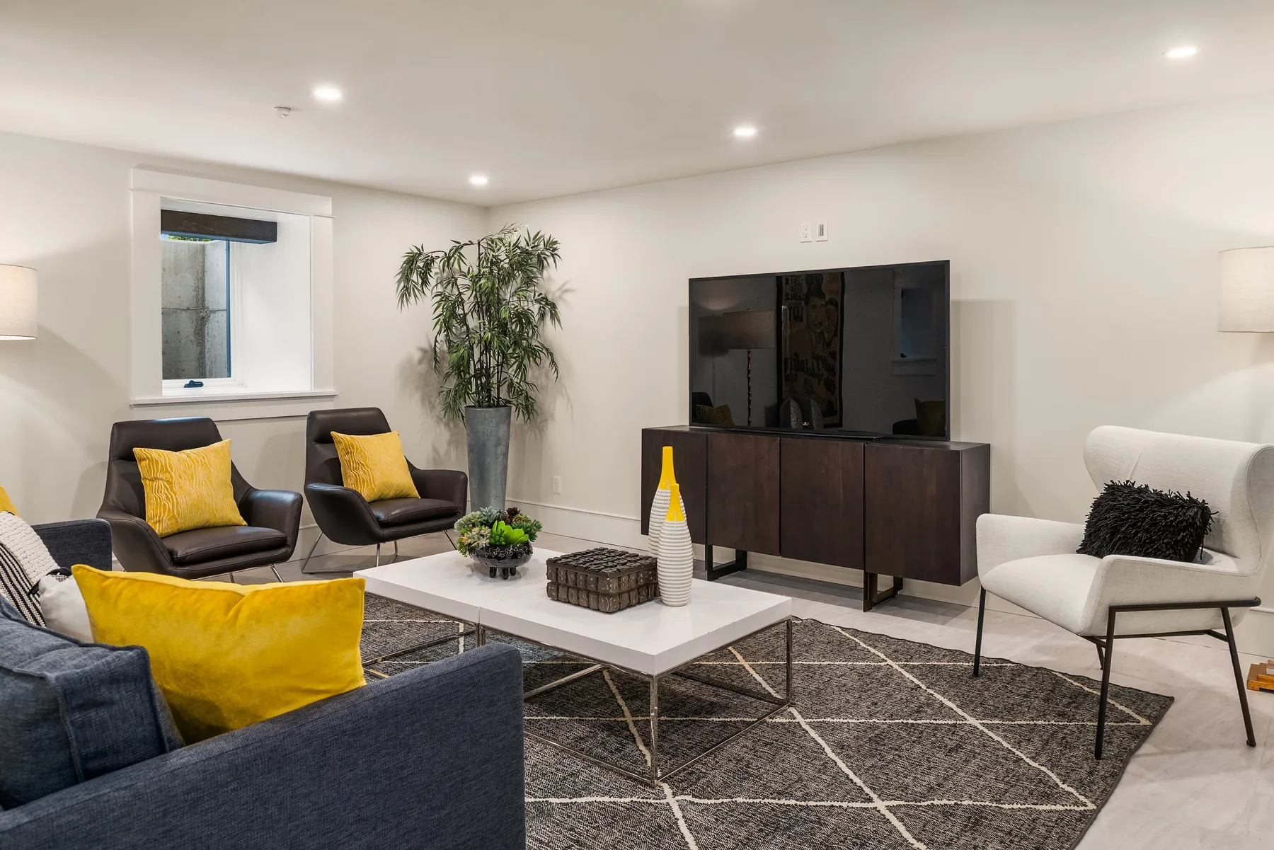 Lower-level lounge staged with charcoal seating, a media console, and bright accents