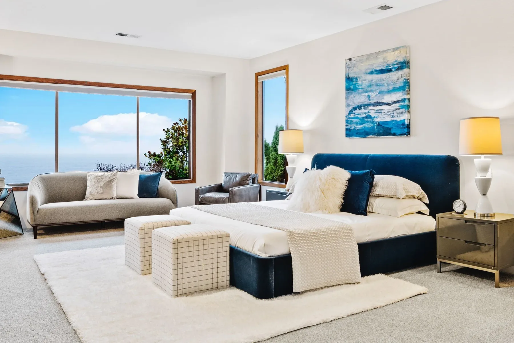 Seattle luxury home staging featuring a serene primary bedroom with an upholstered bed, layered textiles, and water views