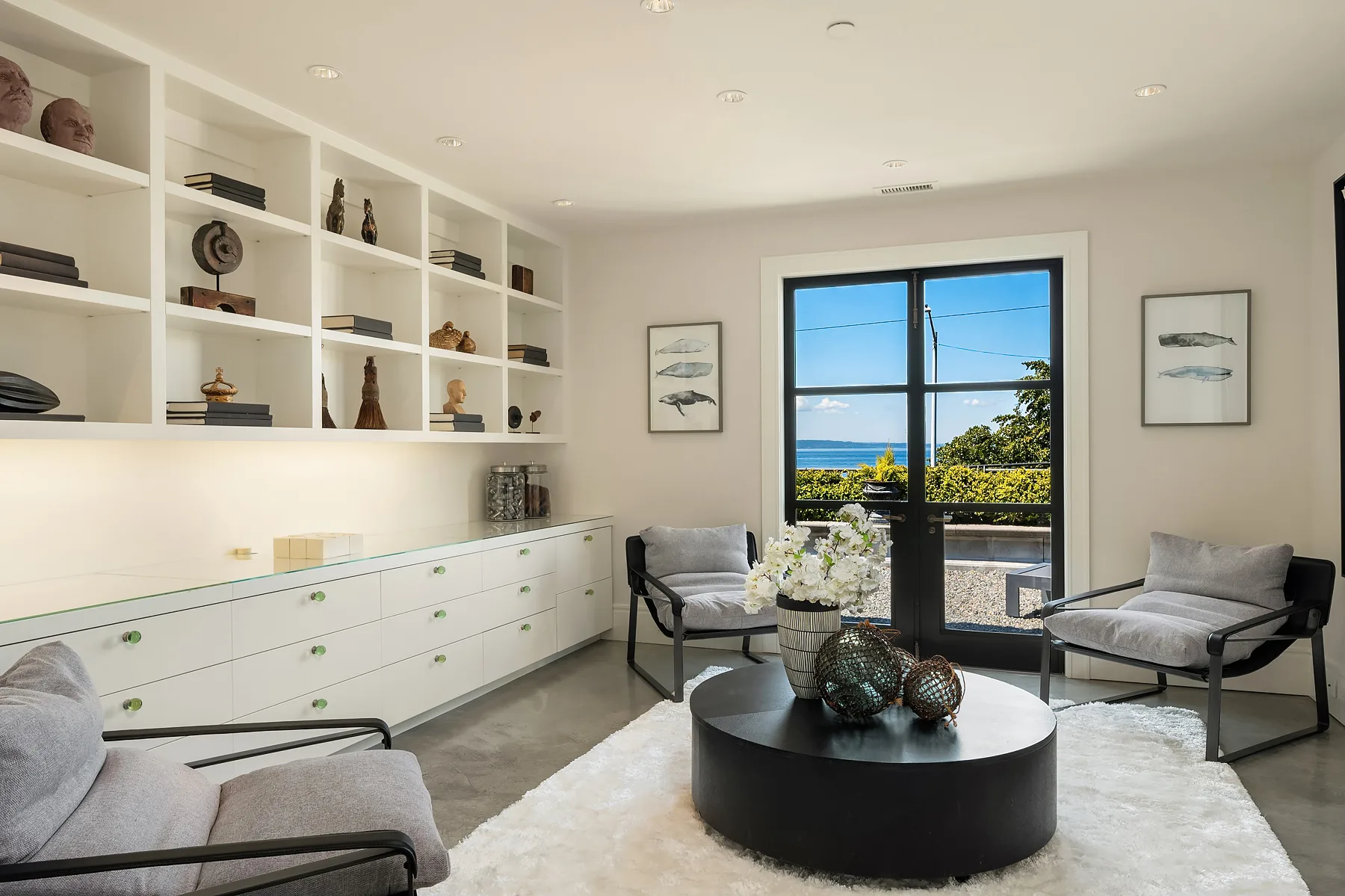 Study with built-in white shelving, grey sling chairs, and French doors opening to a water-view terrace